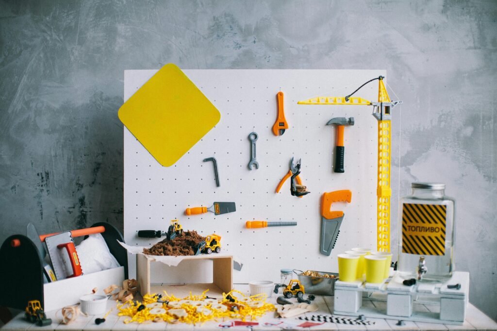 Artistic arrangement of toy tools and construction vehicles on a pegboard backdrop in a workshop setting.